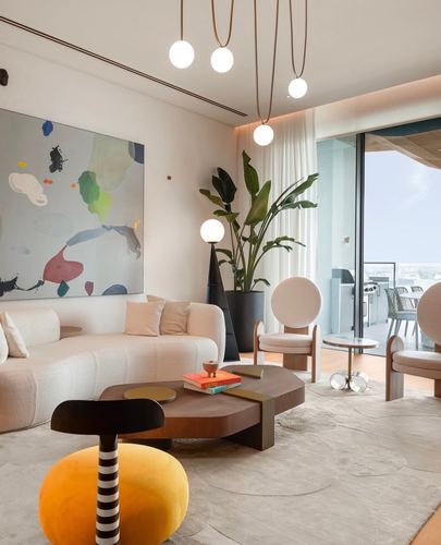 Curved cream sofa and round chairs around a sculptural wood coffee table beside a large window