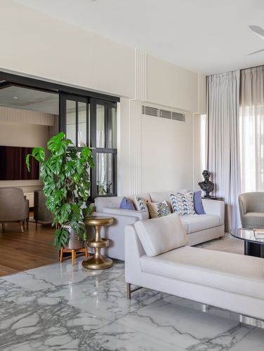 Living room with marble floor, cream sofas, monstera plant, and black-framed glass partition
