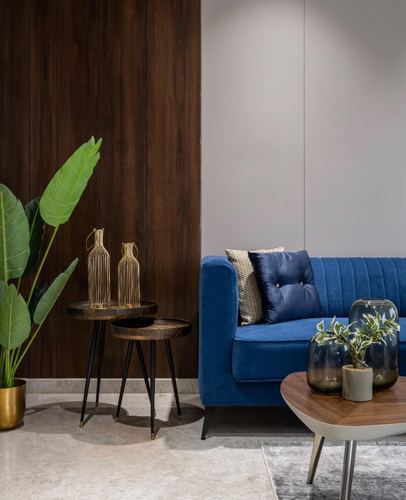 Blue velvet sofa against wood-paneled wall with brass vases and plant