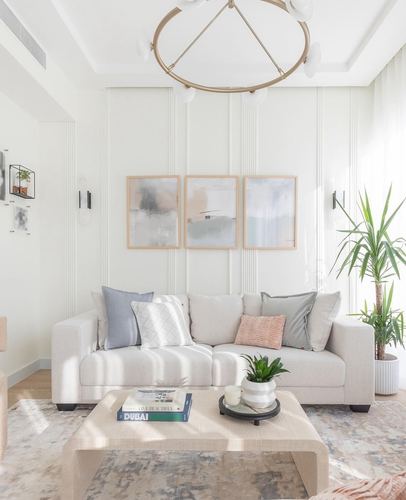 Neutral living room with paneled wall, gallery triptych, beige sofa and round brass chandelier