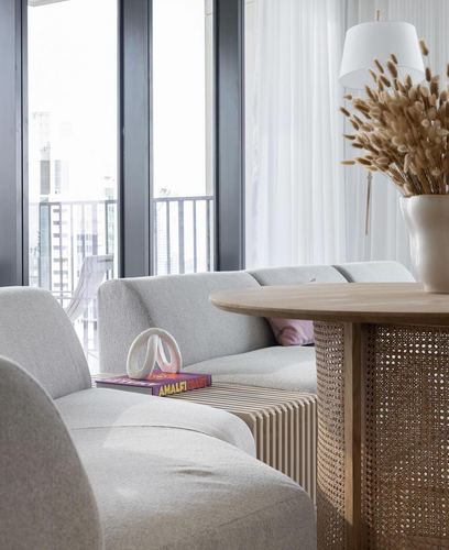 Living room corner with boucle sofa, cane pedestal table, dried grass in vase, city view