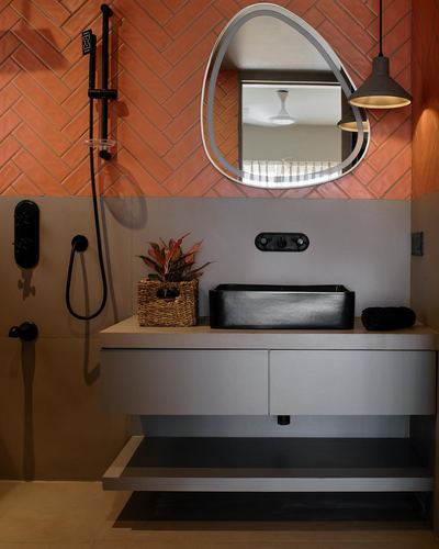 Bathroom vanity with black vessel sink, terracotta herringbone tile, and pear-shaped backlit mirror