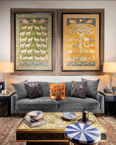 Grey velvet sofa beneath two large framed pichwai paintings, brass coffee table in front