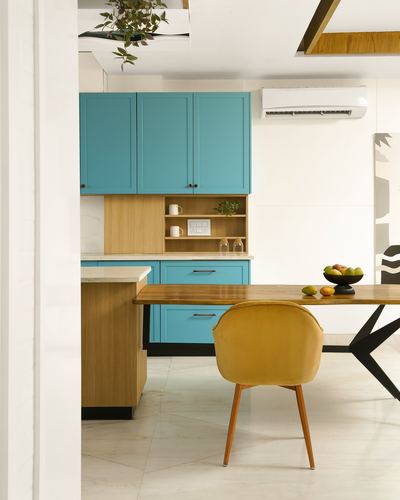 Kitchen with turquoise cabinets, wood island, and mustard velvet chair at dining table