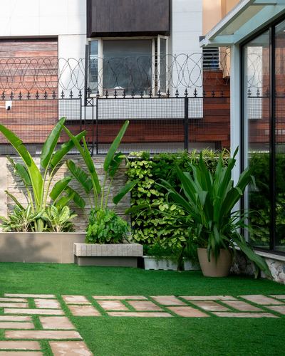 Garden courtyard with potted tropical plants, stone paving, artificial turf, and glass facade behind