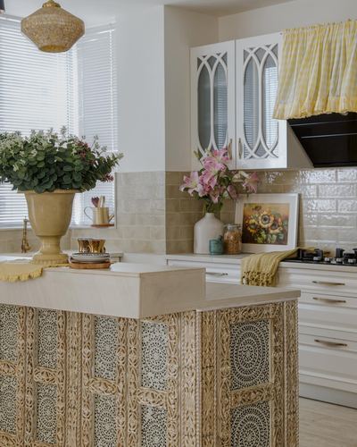 Kitchen island with carved wood front, arched glass cabinets, and yellow gingham curtain in a French country style kitchen