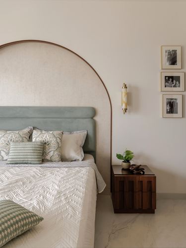 Sage velvet headboard set within an arched wood niche beside a wooden nightstand and brass sconce