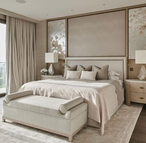Neutral-toned bedroom with upholstered headboard, floral panels, bench, and soft daylight from left window
