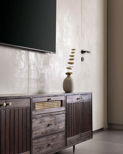 Fluted wood TV console with cane inlay and brass handles against textured plaster wall