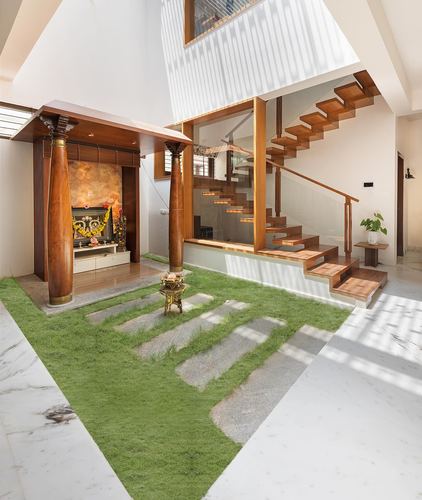 Double-height Bangalore home interior with pooja alcove, wooden staircase, and indoor grass courtyard