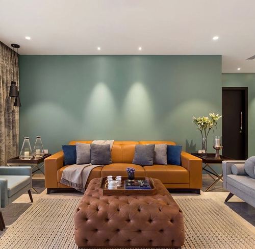 Living room with mustard leather sofa, tufted brown ottoman, and sage green accent wall