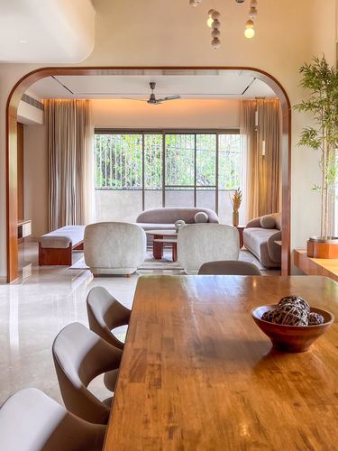 Wood dining table foreground framed by curved archway opening to living room with large window