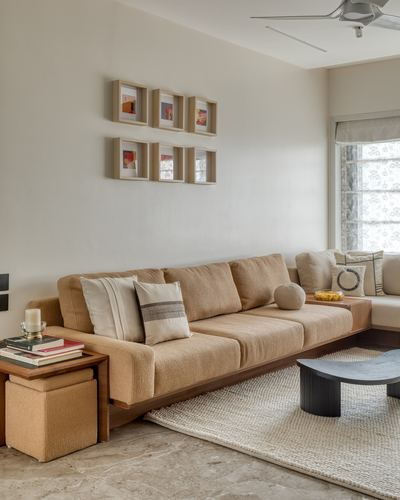 Warm-toned living room with L-shaped sofa, grid of framed art, and round dark coffee table