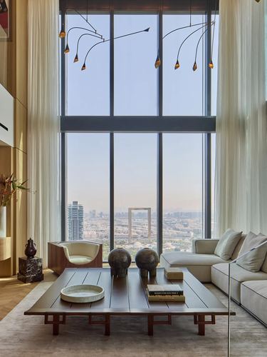 Double-height living room with floor-to-ceiling windows overlooking Dubai skyline, low wooden coffee table and cream sofa
