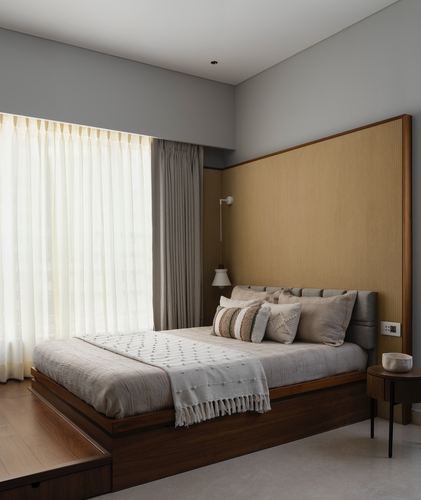 Bedroom with wood platform bed, tall gold fabric headboard wall, and sheer curtained window