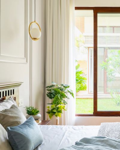 Bedroom corner with globe pendant light, sheer curtains, potted plants and view to garden through wooden-framed glass door