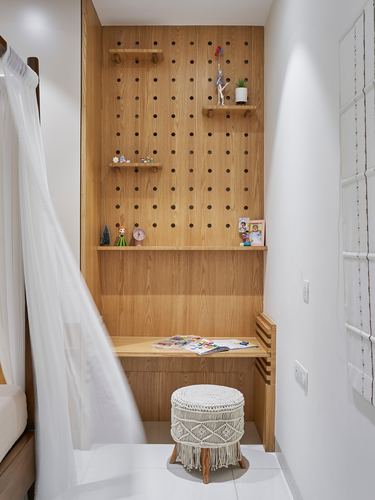 Built-in study nook with wooden pegboard wall, floating shelves with figurines, and macrame stool