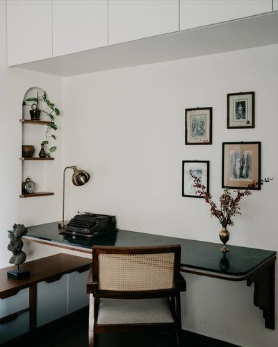 Study nook with stone-top desk, typewriter, brass lamp, cane chair, and framed gallery wall