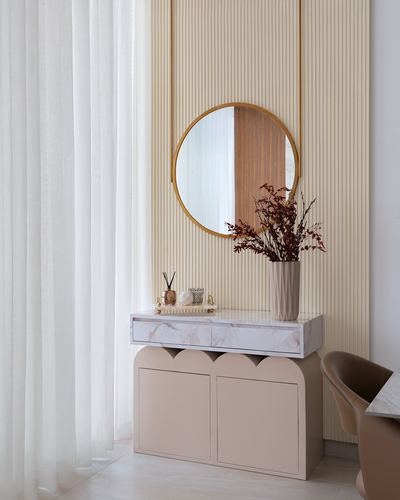 Round brass mirror above marble console with blush scalloped cabinet in foyer