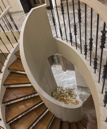 Overhead view of curved wooden staircase with iron railing spiraling above marble floor and gold sculpture