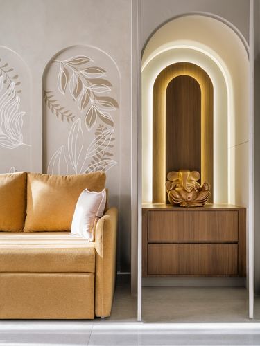 Mustard sofa beside arched wooden pooja niche with lit Ganesha idol on wall panel
