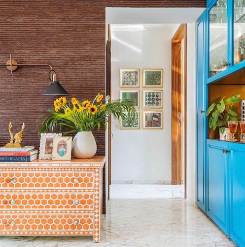 Orange inlay chest of drawers against a textured maroon wall beside a bright blue cabinet and marble hallway