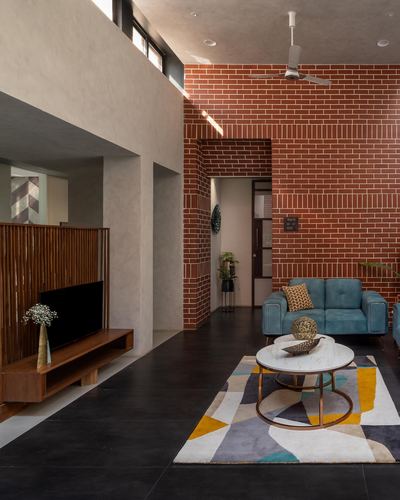Living room with exposed brick wall, teal sofa, round marble table on geometric rug, dark stone floor