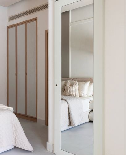 Neutral-toned bedroom with wardrobe, mirrored door reflecting upholstered bed with knit cushions