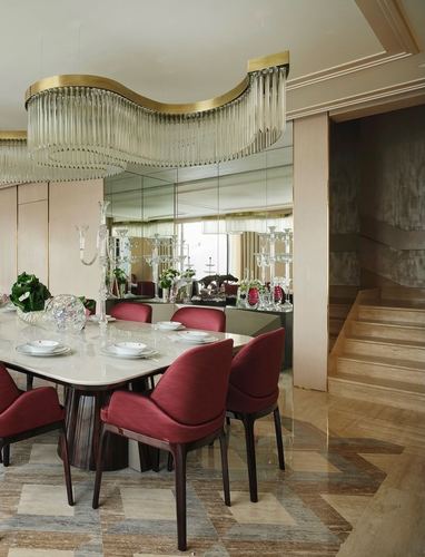 Dining room with wave-shaped glass chandelier, marble table, burgundy chairs, and mirrored wall beside a staircase