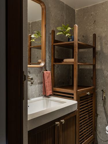 Wooden bathroom shelving unit and arched mirror beside stone-textured sink counter