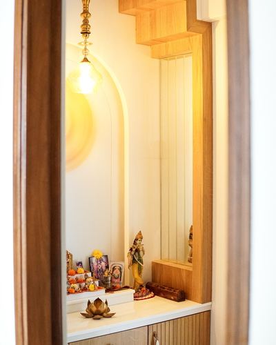 Pooja unit with arched niche, fluted wood panel, brass lamp, and deity idols seen through a doorway