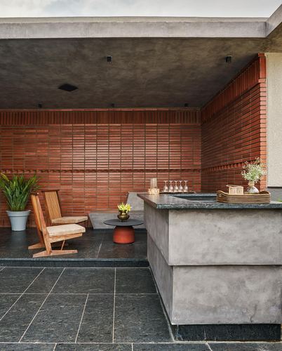 Covered outdoor lounge with ribbed brick wall, concrete bar counter and wooden chairs on stone floor