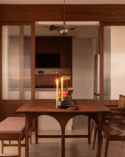 Wooden dining table with lit candles, framed by fluted glass partitions and a view into the kitchen beyond.