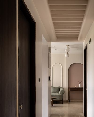Dark wood doors line a corridor leading to an arched mauve alcove with sofa and console