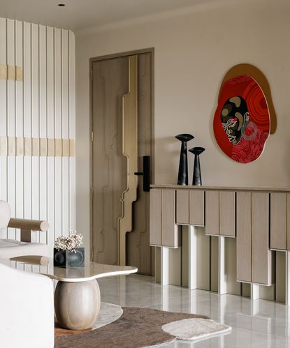 Foyer with fluted door, ribbed console, red sculptural wall art, marble floor and table