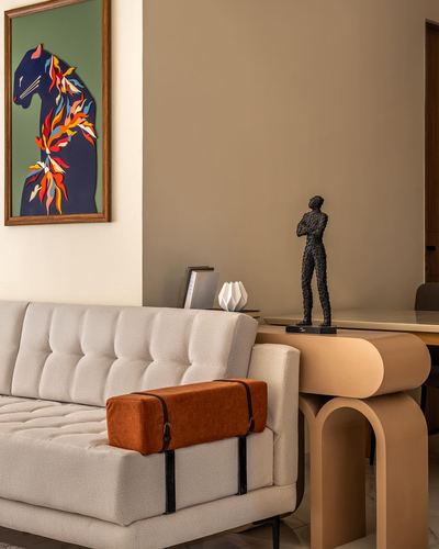 Beige tufted sofa with rust bolster beside a curved console table holding a wire figurine sculpture