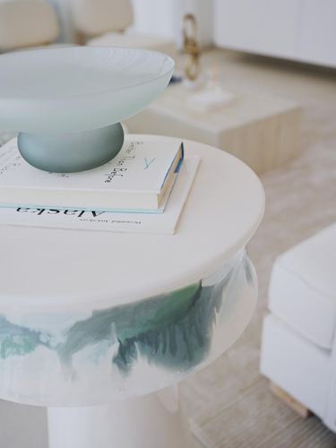 Close-up of a round white side table with painted green edge, holding books and a pedestal bowl