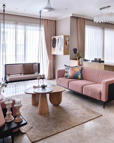 Pink velvet sofa and hanging swing seat in a pastel-toned living room with round wooden tables