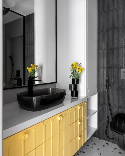 Bathroom vanity with black oval sink, yellow arched cabinet doors, and grey tiled wall