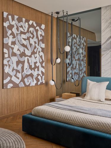 Bedroom with teal upholstered bed, wood-panelled wall, abstract painting, and cluster pendant lights