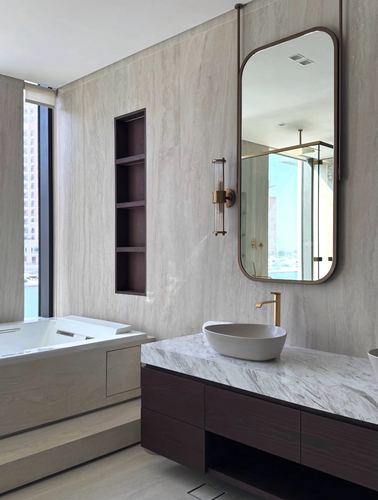 Bathroom with stone wall, marble vanity top, dark wood cabinetry, brass fixtures and city-view window