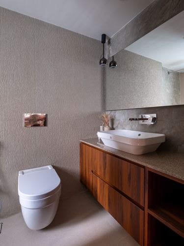 Bathroom with wooden floating vanity, white vessel sink, wall-mounted toilet, and textured stone walls.