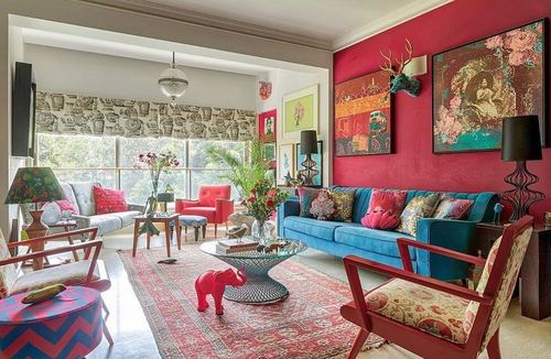 Maximalist living room with magenta wall, teal velvet sofa, layered rugs and colorful cushions