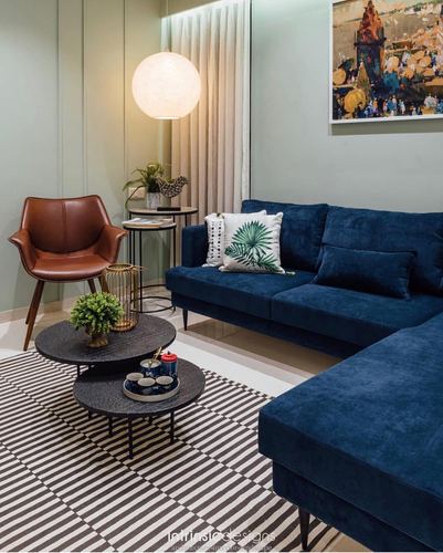 Living room with navy blue velvet sofa, tan leather armchair, striped rug, and globe pendant light