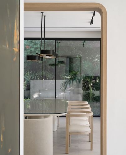 View through arched wooden doorway into minimalist dining room with glass table and greenery beyond