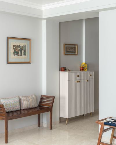 Foyer with fluted pastel cabinet in niche, wooden slatted bench, and framed art