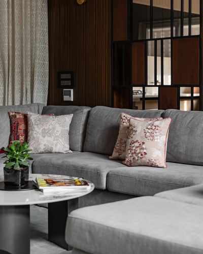 Grey sectional sofa with floral cushions against fluted wood wall and steel partition