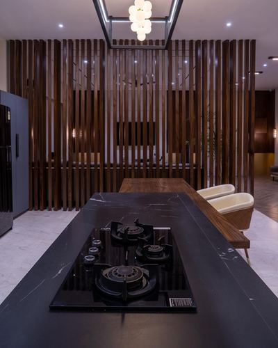 Dark stone kitchen island with built-in gas hob, backed by a vertical wood slat screen and glass pendant light.