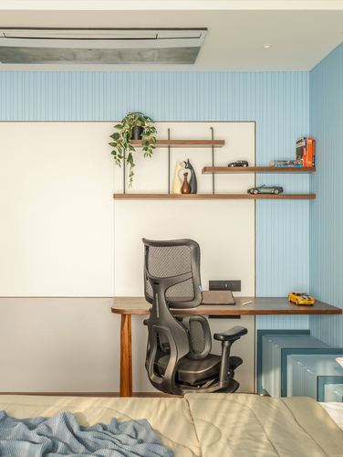 Study nook with mesh office chair, wooden desk, and shelves against blue paneled wall