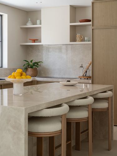 Contemporary kitchen with stone waterfall island, wood cabinetry, and round stools, lemons in glass bowl